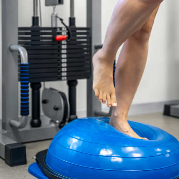 Personne effectuant des exercices d'équilibre sur un ballon Bosu bleu dans una salle de sport.